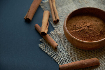 cinnamon sticks, tied with jute rope in rustic style. Ground cinnamon in a wooden bowl and vintage scoop. Close up on a black background. copy space for text. Top view, flat lay.