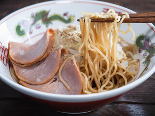 箸で持ち上げた中華麺。チャーシューと玉ねぎをトッピングしたまぜそば。