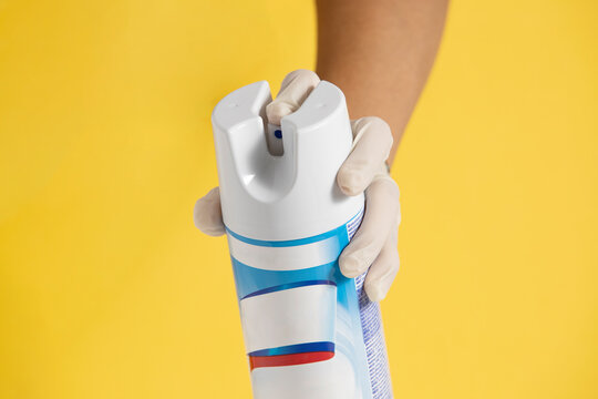 hand wearing a plastic glove sprayed a disinfectant over a yellow background front view