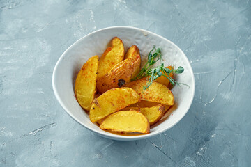 Selyansky baked potatoes in spices in a white bowl on a gray background. Baked potato wedges