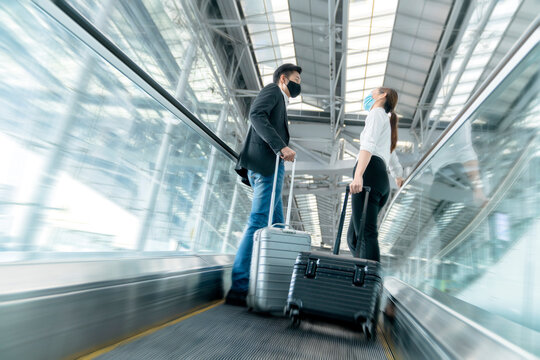 two asian business partners with face mask protection social distancing new normal lifestyle Business travellers walking in airport with luggage motion movement