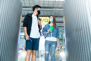 young Asian male and female couple tourists drag luggages walking through the hallway after arrival ,two asian people traveller wearing facial face mask virus protection safety travel ideas concept