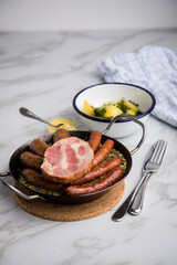Oldenburger Grünkohl mit Pinkel, Kohlwurst, Kassler Schweine Nacken, Senf und Kartoffeln in Gusseisen Pfanne auf Marmor Tisch