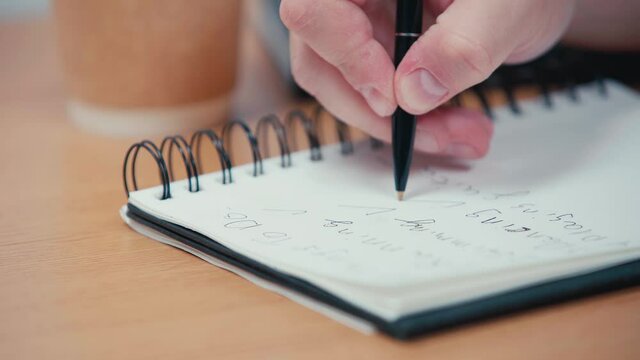 Selective focus of man writing on spiral notebook 