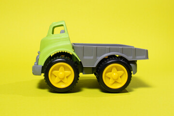 Toy truck car on a yellow background - construction equipment for children. Bright children's plastic toys, dump truck childhood.