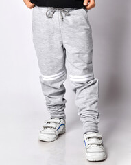 Closeup of kid in grey sport pants trousers with white stripes and white sneakers. Front view
