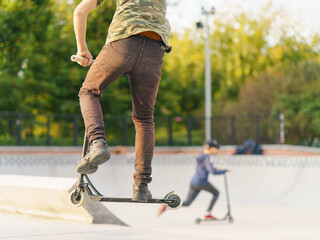 Teenager performs a trick in the city skate  park. Push scooter. He jumping over an obstacles. Extreme sports is very popular among youth. Legs and push scooter photography