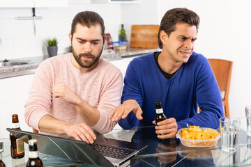 Friendly male meeting over beer at home, men looking at laptop and discussing. High quality photo