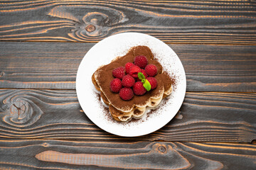 portion of Classic tiramisu dessert with raspberries on ceramic plate on wooden background