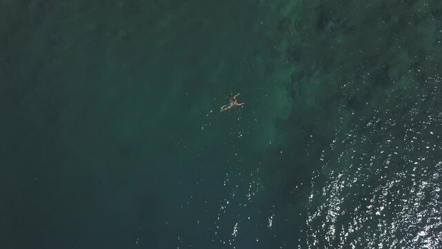 Top down aerial view of young man in short and mask swimming in ocean on summer.