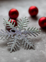 Christmas decorations on a gray background. A silver snowflake surrounded by unfocused burgundy Christmas balls, Christmas toys and stone ornament. Top view.