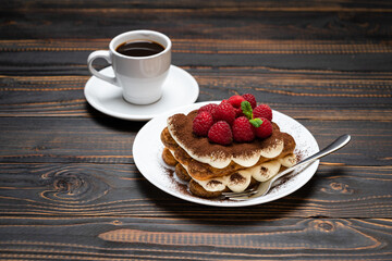 portion of Classic tiramisu dessert with raspberries and cup of espresso coffee isolated on wooden background