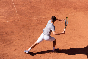 Professional tennis player performs forehand hit on clay tennis court. Young male athlete with...