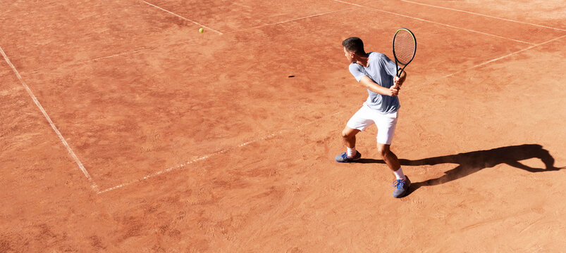Tennis player playing on clay court. Young male tennis player hitting backhand kick. Professional athlete is concentrating in the game. Sports background. Banner. Copy space for text