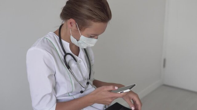 A female doctor dials a message on her phone and looks at a picture of a sick covid-19 lung