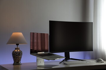 Computerarbeitsplatz mit einem flachen Laptop und einem gekrümmten und großen 4k Monitor mit Hintergrundbeleuchtung auf einem weißen Tisch.
