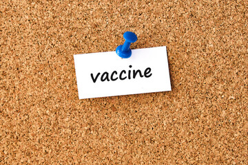 Vaccine. Word written on a piece of paper, cork board background.