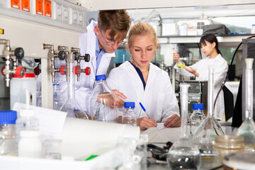 Fototapeta premium Two students of Faculty of Chemistry performing experiments in university laboratory, recording results in workbook