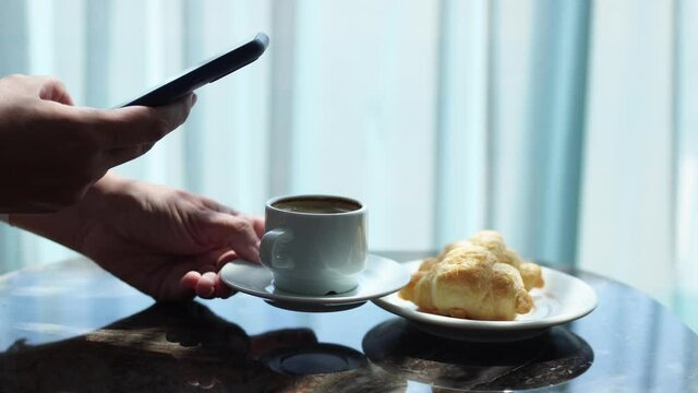Closeup side view of woman holding modern smartphone and taking pictures of her morning breakfast coffee and tasty croissants buns to share photos on social media resources