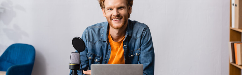 panoramic shot of excited redhead broadcaster looking at camera near microphone