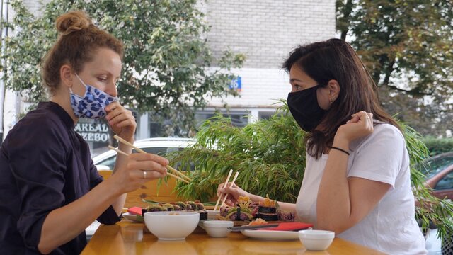 Two young women having sushi lunch wearing face masks during second wave of covid-19 pandemic