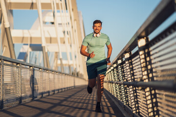 Young happy man is jogging outdoor on bridge in the city.