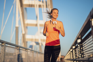 Young happy woman is jogging outdoor on bridge in the city.