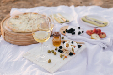 Fototapeta na wymiar Summer picnic at sunset on beach with white wine, pizza, cheese, olives and fresh fruits.