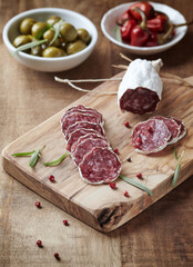 Sliced french salami with fresh rosemary and olives on rustic wooden background.