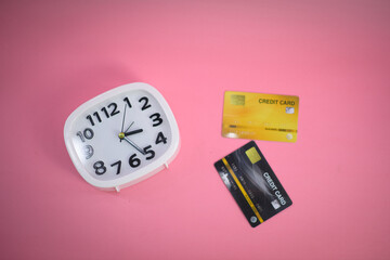 White clock with a credit card on a pink pastel background. Top view