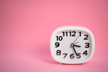 White wall clock with pink second hand hanging on the wall. Minimalist flat lay image of plastic...
