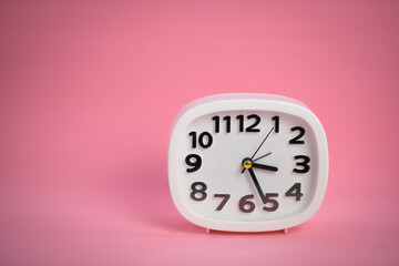 White wall clock with pink second hand hanging on the wall. Minimalist flat lay image of plastic wall clock over blue turquiose background with copy space and central composition
