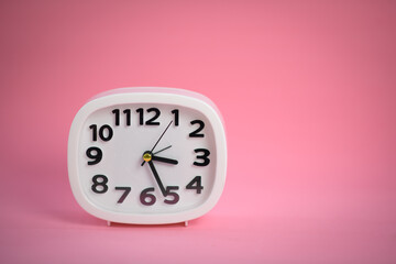 White wall clock with pink second hand hanging on the wall. Minimalist flat lay image of plastic wall clock over blue turquiose background with copy space and central composition