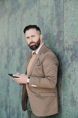 Portrait of bearded businessman in suit looking at camera while working on the phone in the city