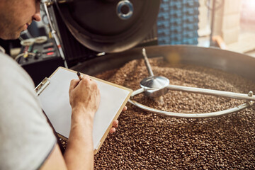 Male worker taking notes while using coffee roasting machine