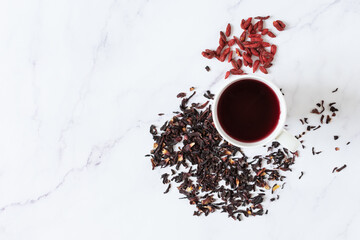 Obraz na płótnie Canvas Red Hibiscus tea in glass mug and goji berries top view on white marble background.