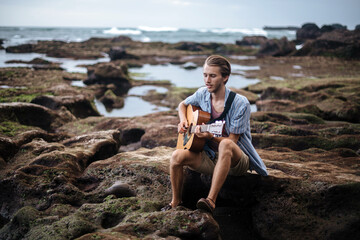 Romantic young man with a guitar on the beach
