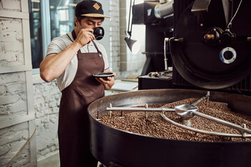 Male worker drinking coffee near coffee roasting machine