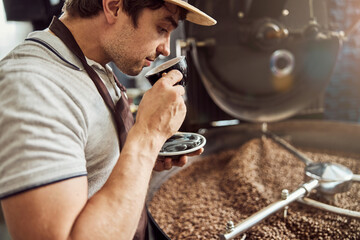 Handsome man drinking coffee near coffee roasting machine