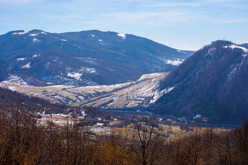 mountainous countryside in early spring. dry grass and leafless trees on the hillside. snow in the distant valley and ridge