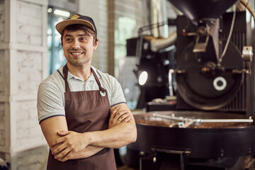 Cheerful male worker standing near coffee roasting machine