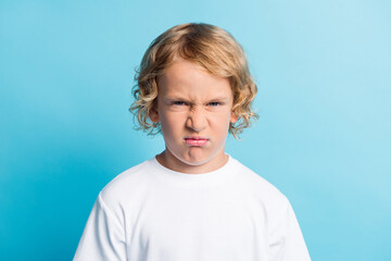 Portrait of little boy with grimace face feel disappointed wear white t-shirt isolated over blue...