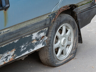 Fototapeta na wymiar Wheel with a deflated tire on an abandoned rusty car close-up.