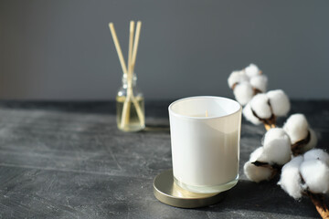 hygge and aromatherapy concept. aroma reed diffuser, branch of cotton and white soy candle on grey table at home. minimal style composition. winter and autumn mood