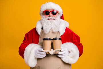 Close-up portrait of his he nice attractive cheerful grey-haired Santa waiter wearing apron holding in hands two paper cups order latte isolated bright vivid shine vibrant yellow color background