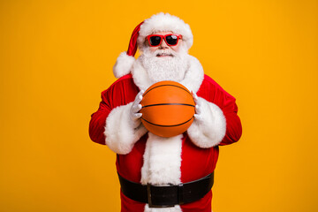 Fototapeta na wymiar Portrait of his he nice attractive cheerful cheery sporty Santa holding in hands orange ball season team league isolated over bright vivid shine vibrant yellow color background