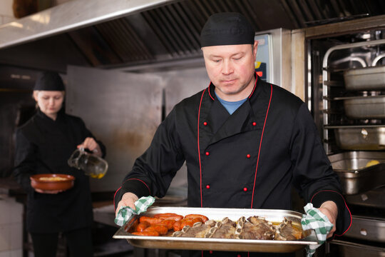 Skilled cook presenting appetizing baked pork ribs and sausages in restaurant kitchen, ready to serve it to guests