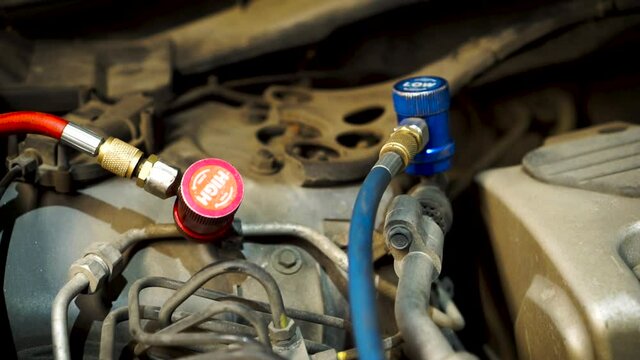 Refueling a car air conditioner in an old workshop. Footage. Auto repair with beautiful red and blue pressure pipes