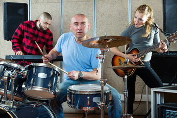 Rehearsal of the music group. Rock band with emotional male drummer playing in a recording studio