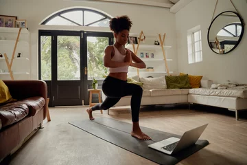 Crédence de cuisine en verre imprimé École de yoga Femme africaine en bonne santé regardant une vidéo sur un ordinateur portable tout en faisant de l& 39 exercice avec les mains jointes sur un tapis de yoga à la maison